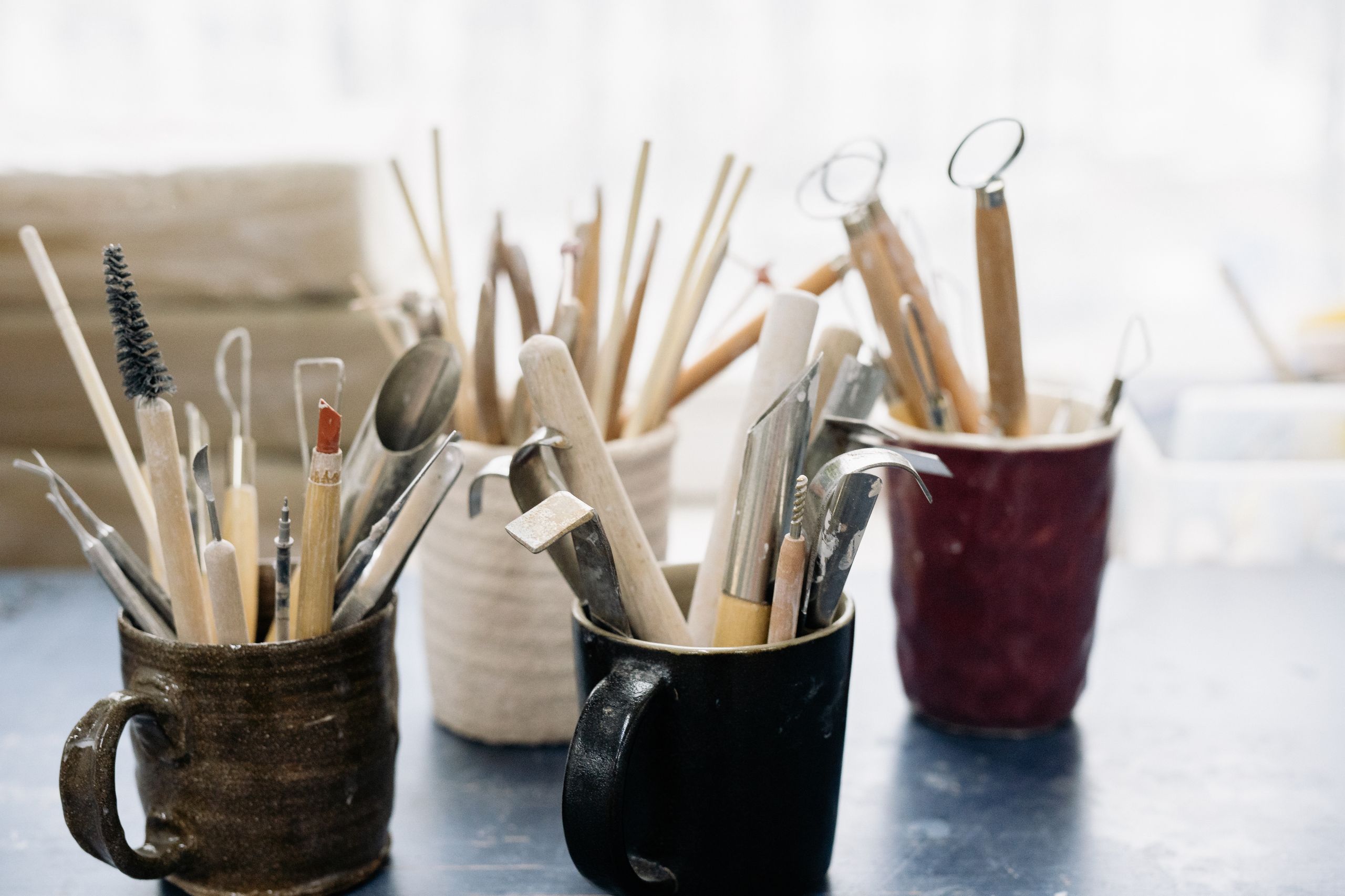 A collection of pottery tools in mugs on a workshop table, perfect for crafting enthusiasts.